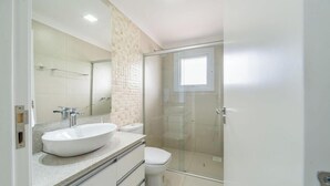 A modern bathroom with a large white sink, a toilet, and a glass-enclosed shower. - NSA - Apartments Close to the Center of Canela RS (Canela)