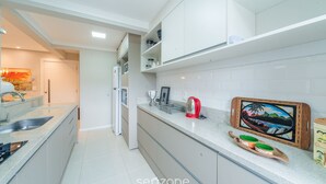 A modern kitchen with white cabinets, granite countertops, and a built-in oven. There is a red kettle and a framed picture on the counter. - NSA - Apartments Close to the Center of Canela RS (Canela)