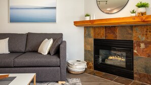 Una sala de estar con un sofá gris, una chimenea, un espejo redondo y un cuadro en la pared.