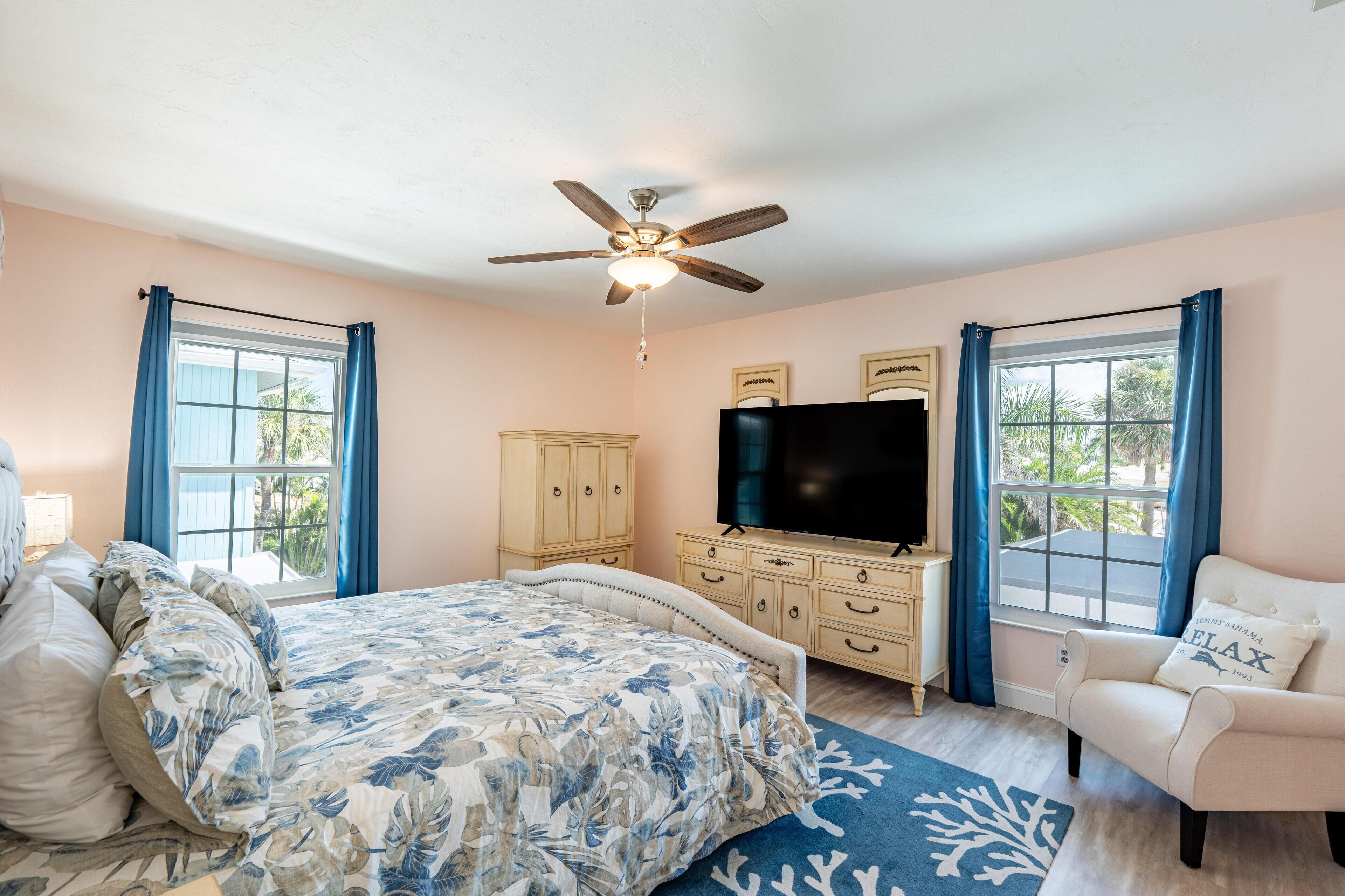 A bedroom with a bed, a TV, a ceiling fan, and a window with curtains.