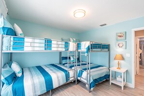 Una camera con letto a castello, parete azzurra, un piccolo comodino con lampada e una porta che dà su un'altra stanza.