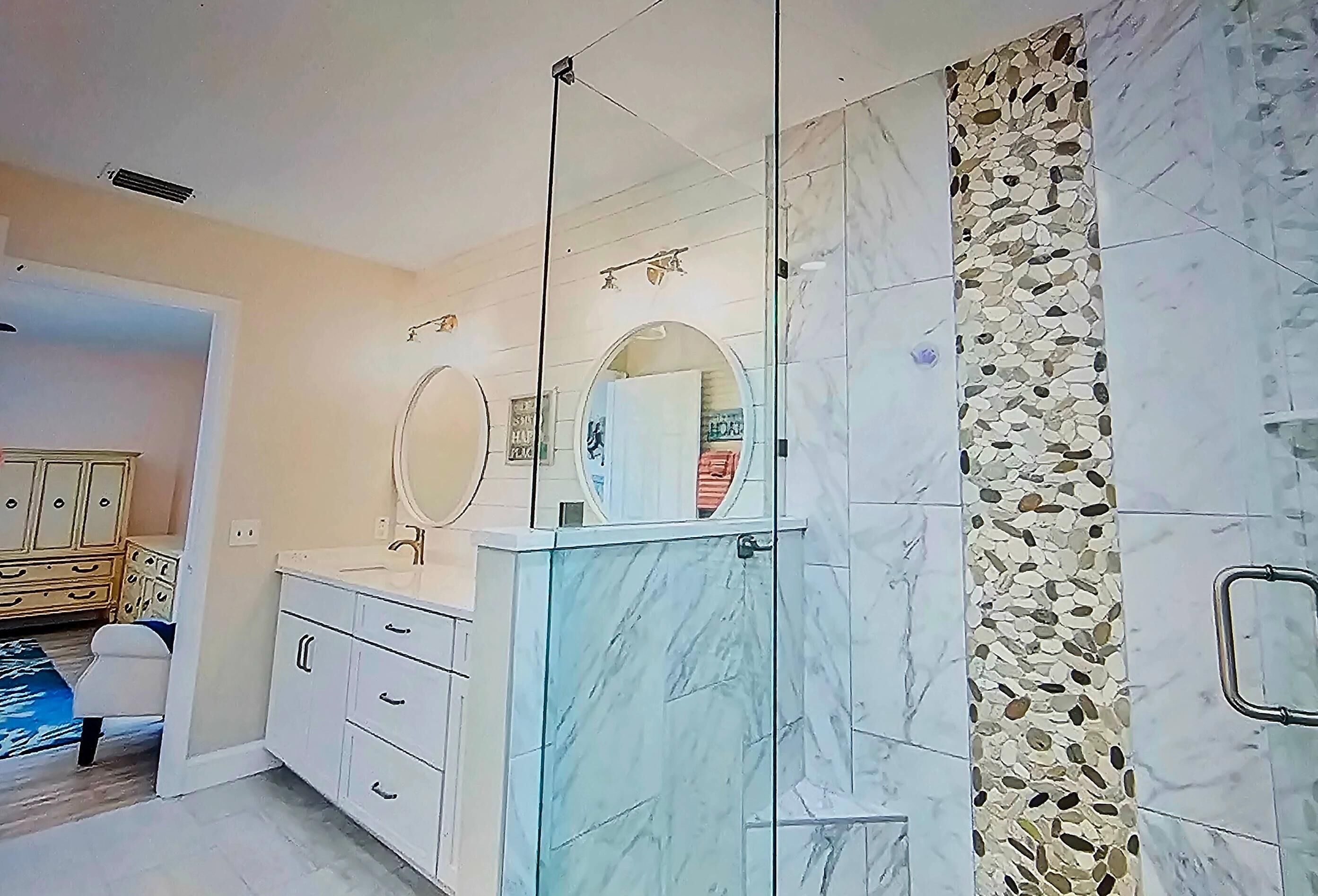 A bathroom with a glass shower enclosure, a marble vanity, and a decorative wall.