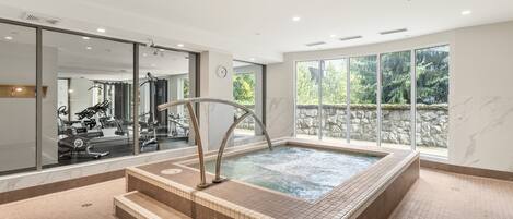 A spa area with a hot tub, exercise equipment, and large windows.