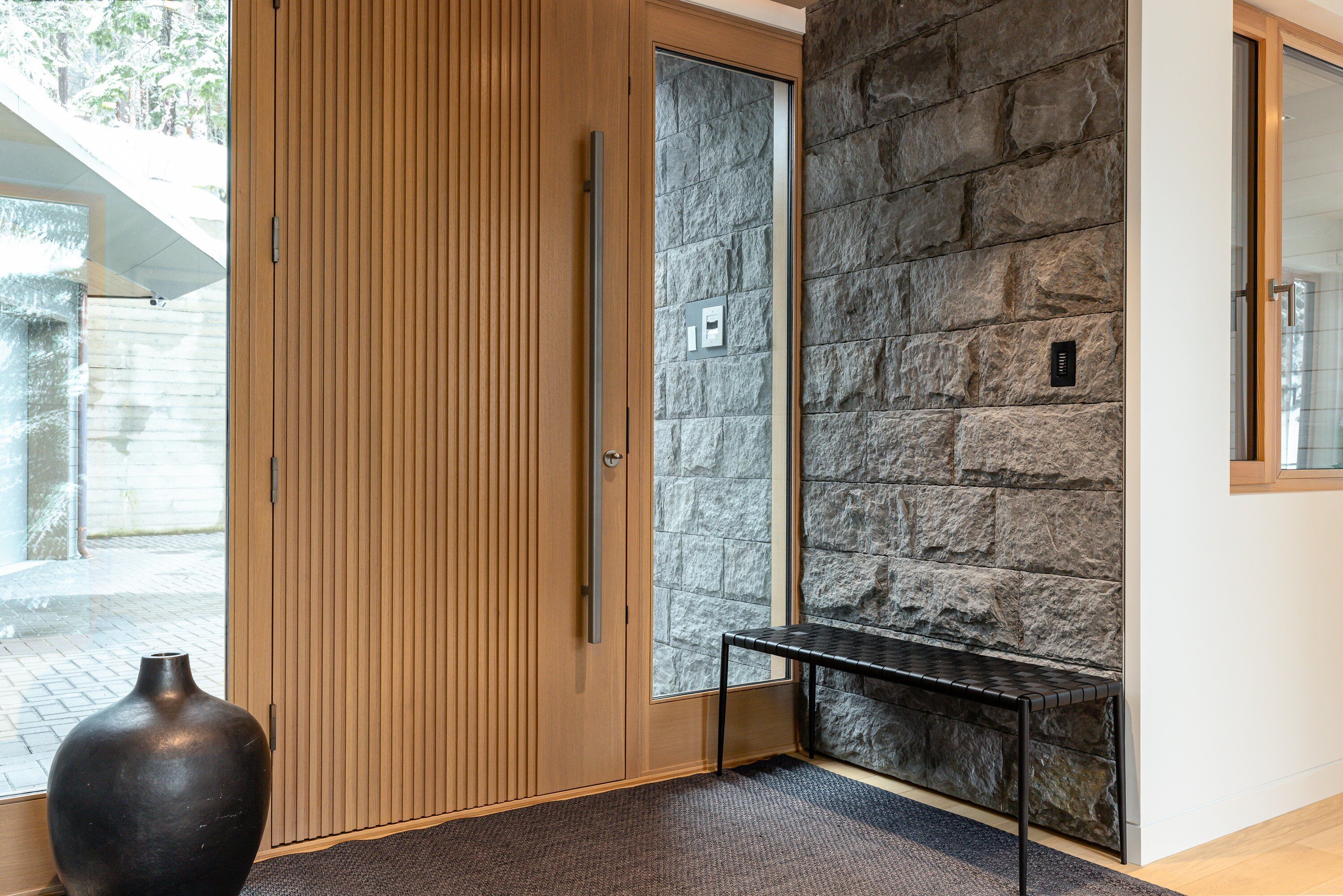Una habitación con puerta de madera, pared de piedra, un banco y un jarrón grande.