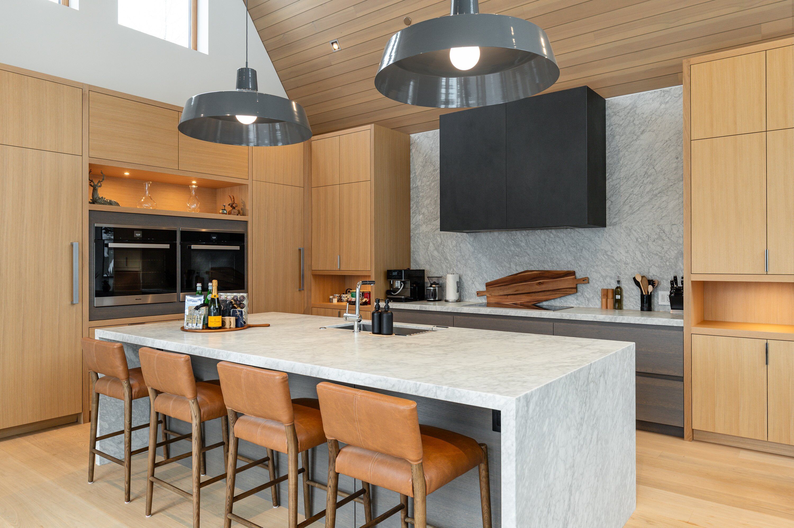 A modern kitchen with a large island, wooden cabinets, and pendant lighting.