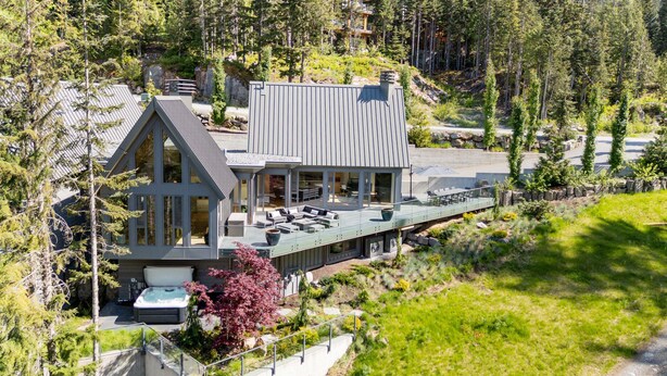 Une maison moderne dotée d’une grande terrasse, d’un jacuzzi et offrant une vue sur la forêt environnante.