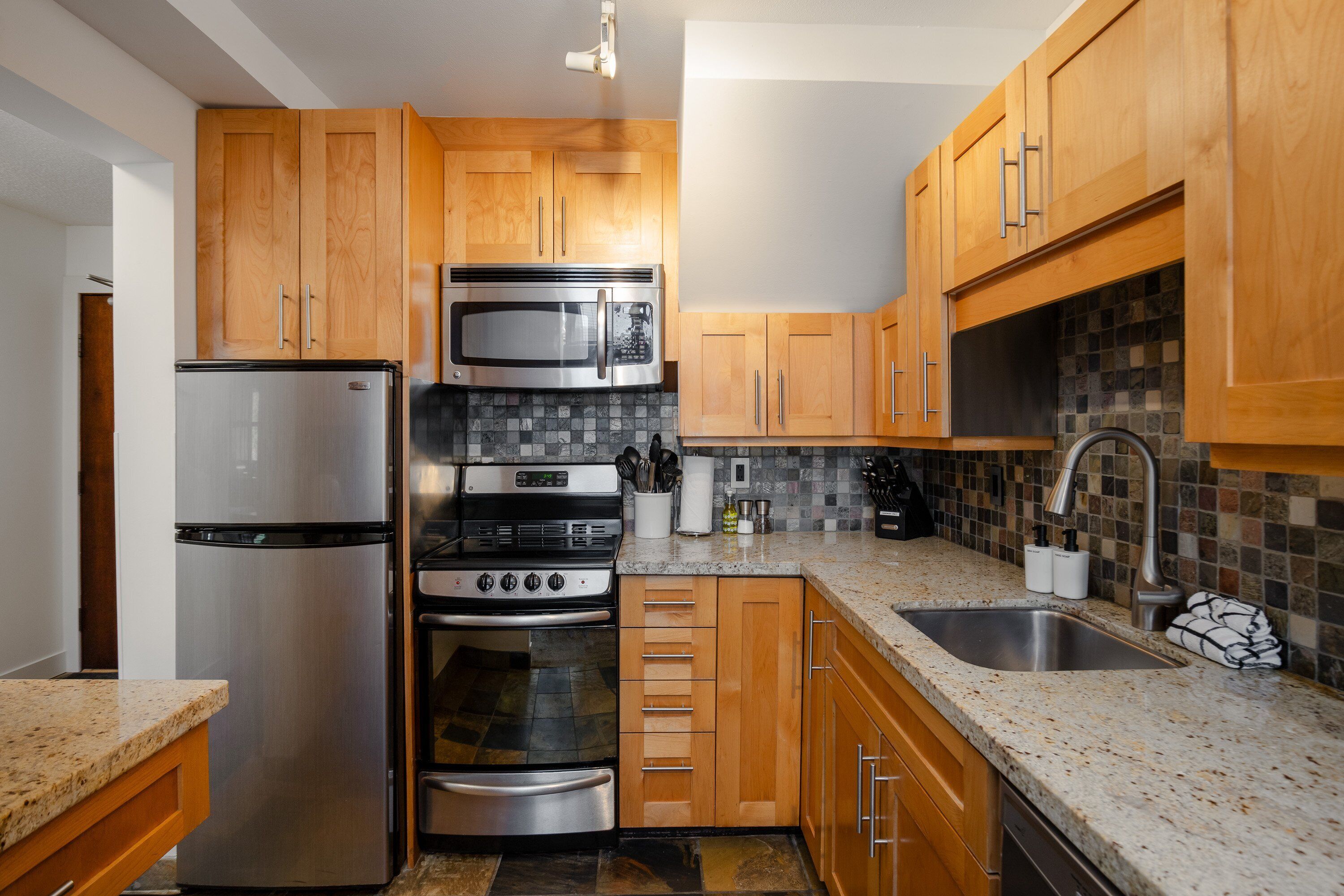 A kitchen with wooden cabinets, stainless steel appliances, a granite countertop, and a tiled backsplash.