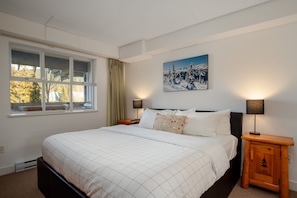 Ein Schlafzimmer mit einem Bett, einem Fenster, einem Gemälde und zwei Nachttischlampen.