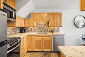 A kitchen with wooden cabinets, a microwave, stove, and dishwasher. - Crystal Suite at Glacier Lodge (Whistler)
