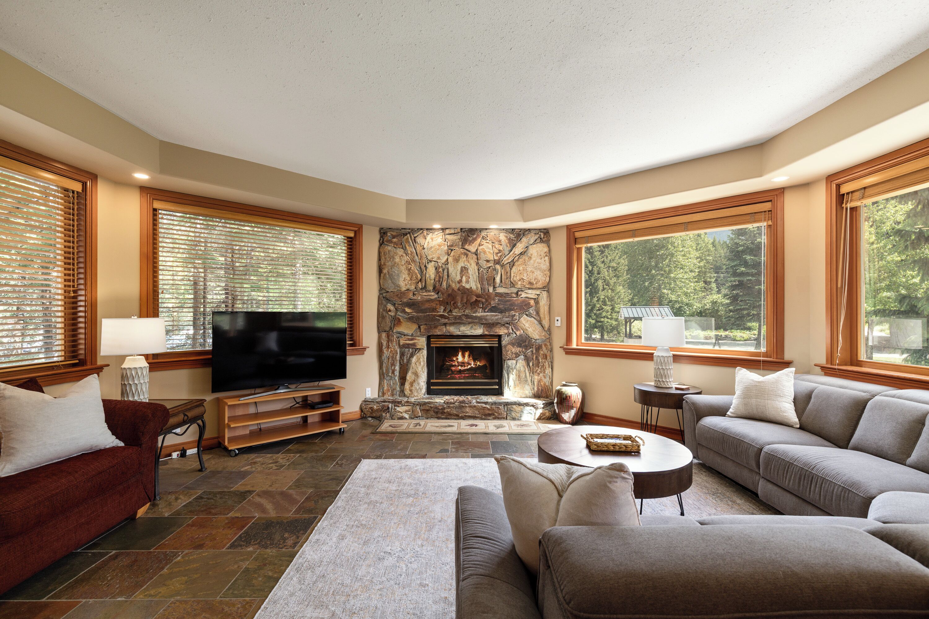 Una sala de estar con chimenea de piedra, televisor y ventanas amplias.