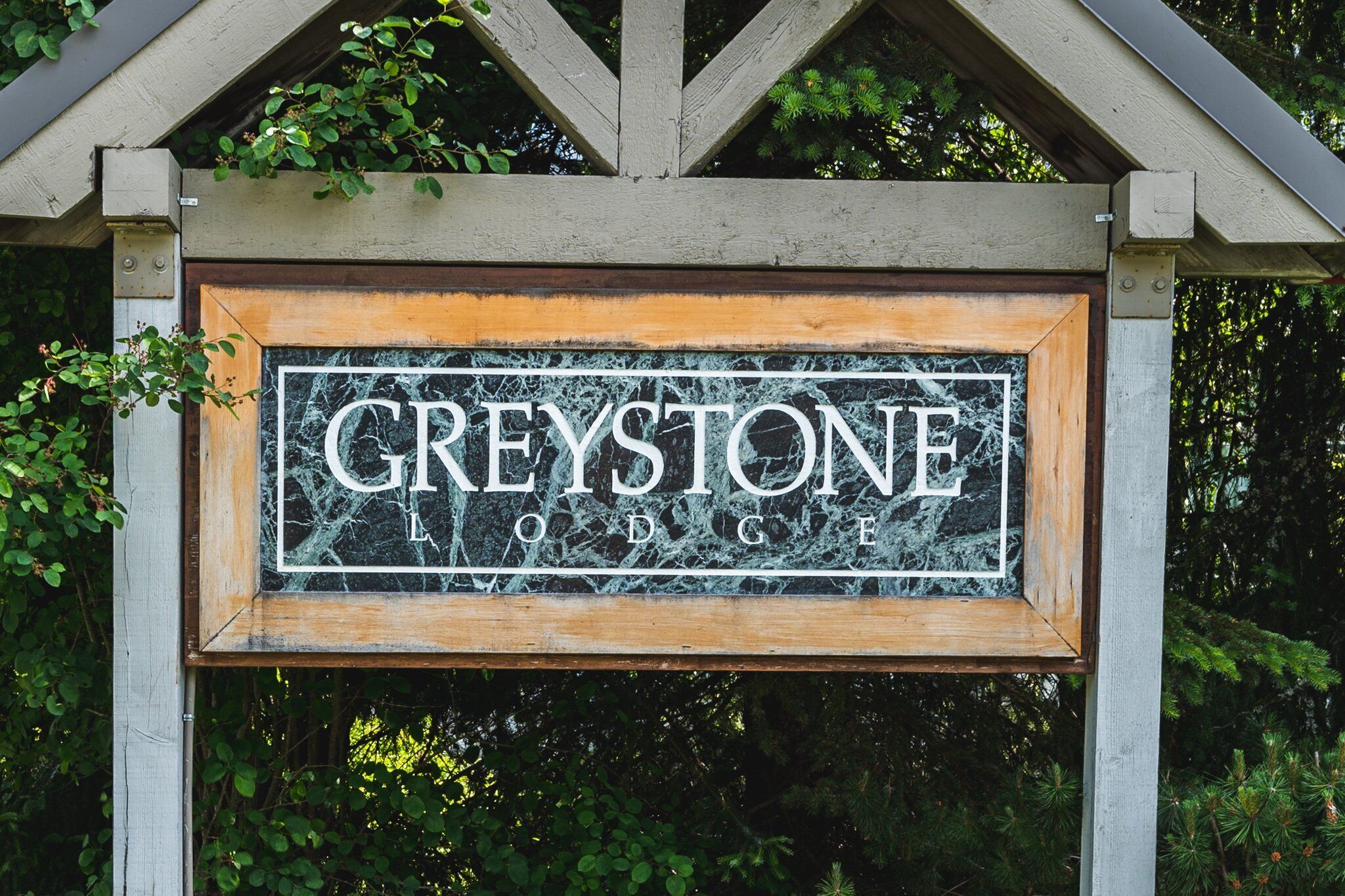 Une enseigne en bois portant l’inscription « GREYSTONE LODGE » est fixée sur une structure surmontée d’un toit triangulaire.