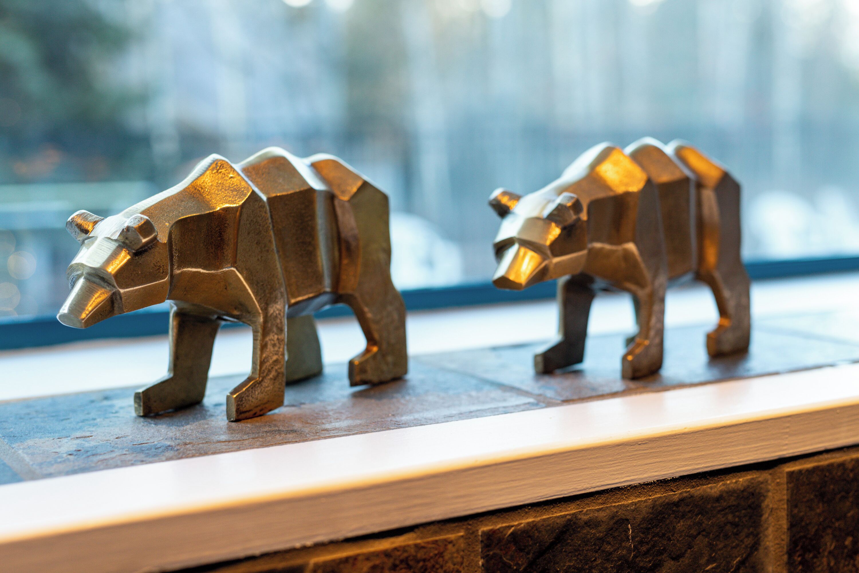 Dos esculturas metálicas de osos sobre un repisa de madera.