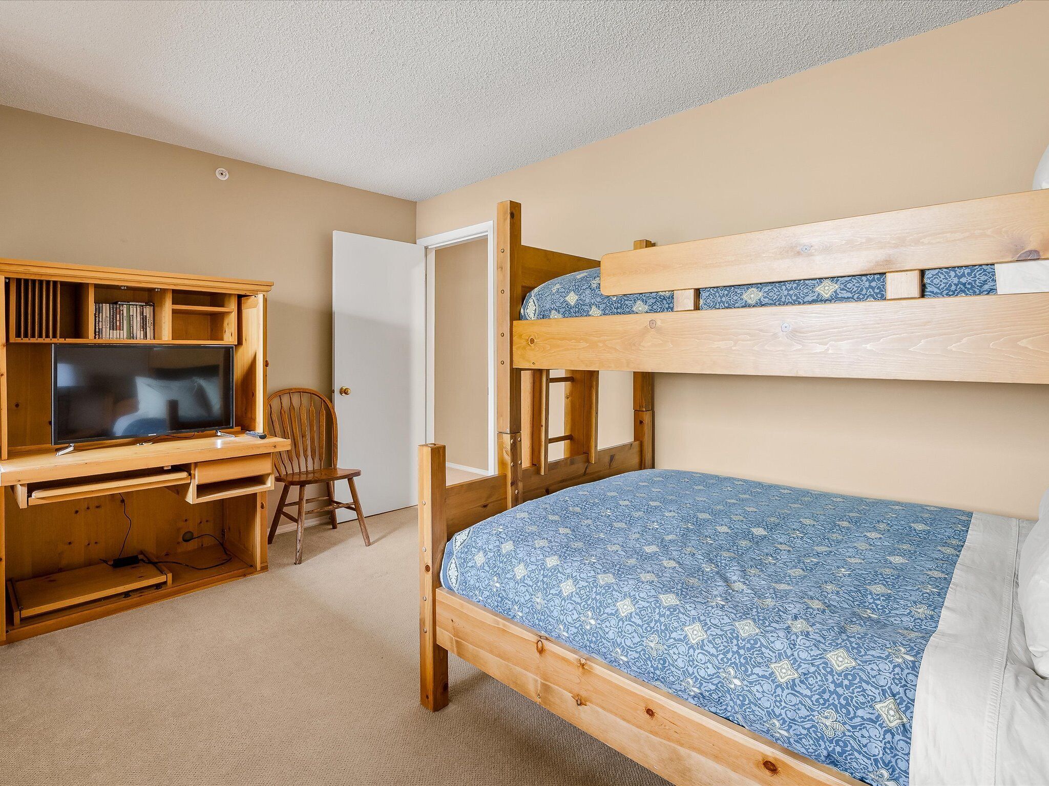 A bunk bed with a patterned mattress, a wooden desk with a television, and a bookshelf.