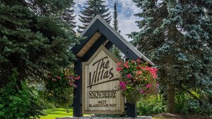 A wooden sign with 'The Villas' and 'Snowberry' written on it, placed on a stone base with a stone wall behind it. - Glacier Suite at Snowberry (Whistler)