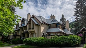 A large, multi-story house with a prominent chimney, surrounded by lush greenery and a well-maintained lawn. - Glacier Suite at Snowberry (Whistler)