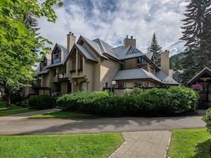 A large, multi-story house with a prominent chimney, surrounded by lush greenery and a well-maintained lawn. - Glacier Suite at Snowberry (Whistler)