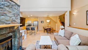 A spacious living area with a stone fireplace, a dining table with chairs, a sofa, and a staircase leading to an upper level. - Glacier Suite at Snowberry (Whistler)