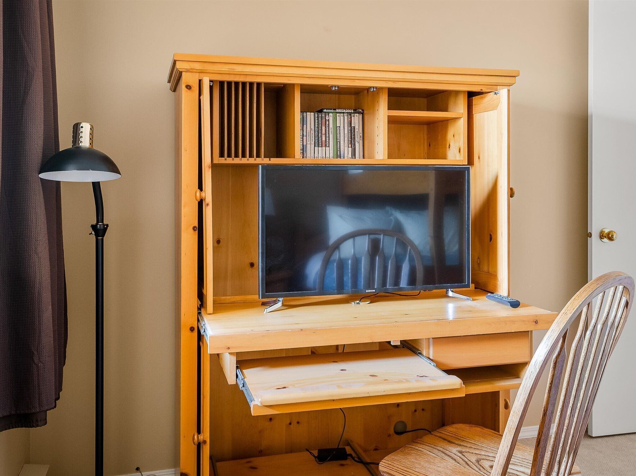 Un escritorio de madera con una televisión de pantalla plana, una lámpara y una silla.