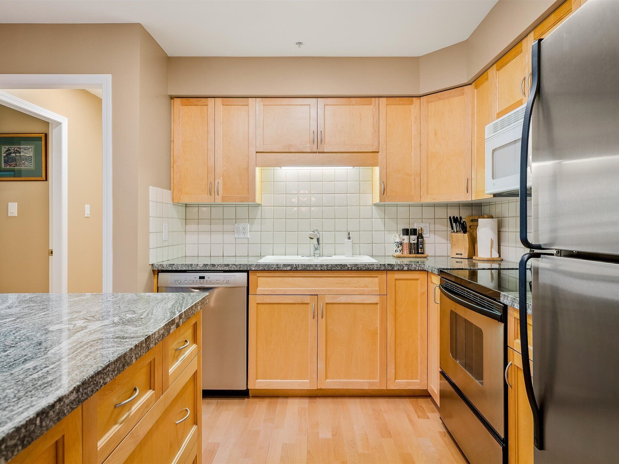 A modern kitchen with wooden cabinets, a stainless steel refrigerator, a dishwasher, and a tiled backsplash.