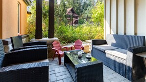 Un patio al aire libre con muebles de mimbre, una mesa con superficie de vidrio y vista a una casa a través de una cerca.