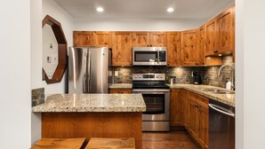 Una cocina con gabinetes de madera, electrodomésticos de acero inoxidable, encimeras de granito y una isla integrada con taburetes.