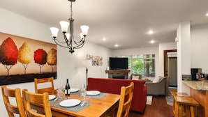 Un comedor con mesa y sillas de madera, una lámpara de araña y un cuadro de árboles en la pared.