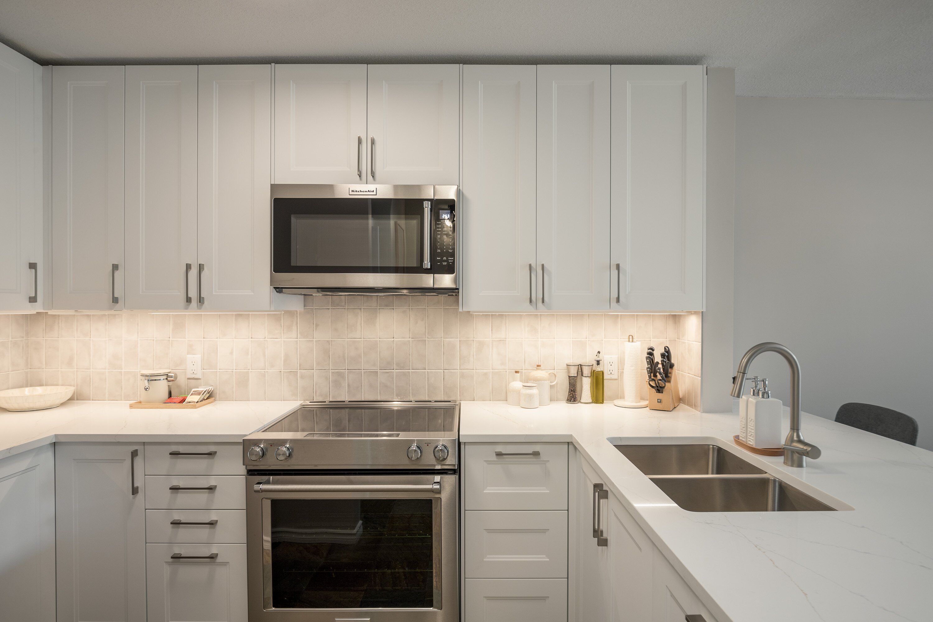 A modern kitchen with white cabinets, stainless steel appliances, and a double sink.