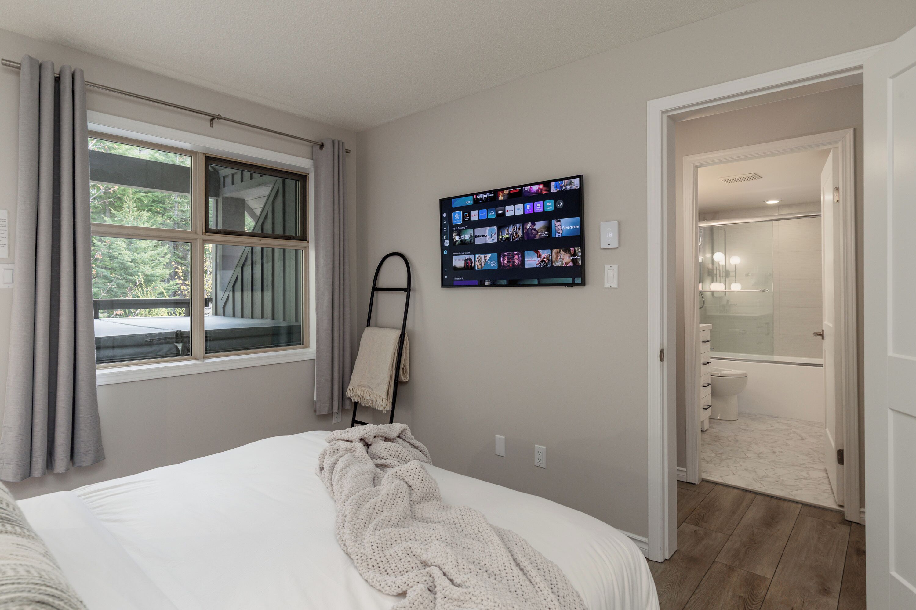 Une chambre à coucher avec un lit, un téléviseur fixé au mur et une vue sur l’extérieur par une fenêtre.