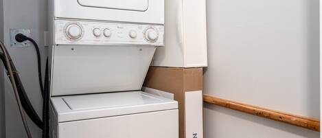 A white washing machine with control knobs and a hose, a wooden beam, and a cardboard box labeled 'MOEN' against a wall.