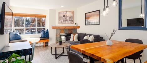 A modern living room with a dining area, a fireplace, and a large window with a view.