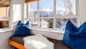 A room with a bench against a window, a white furry rug, and blue cushions. - Mountain View Suite at Marketplace Lodge (Whistler)