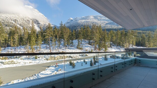 A balcony with a glass railing overlooking a snowy landscape with trees and mountains. - Nature's Nook at Wedgewoods (Whistler)