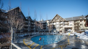 Une piscine où une personne nage, entourée de bâtiments dotés de balcons, sous un ciel dégagé.