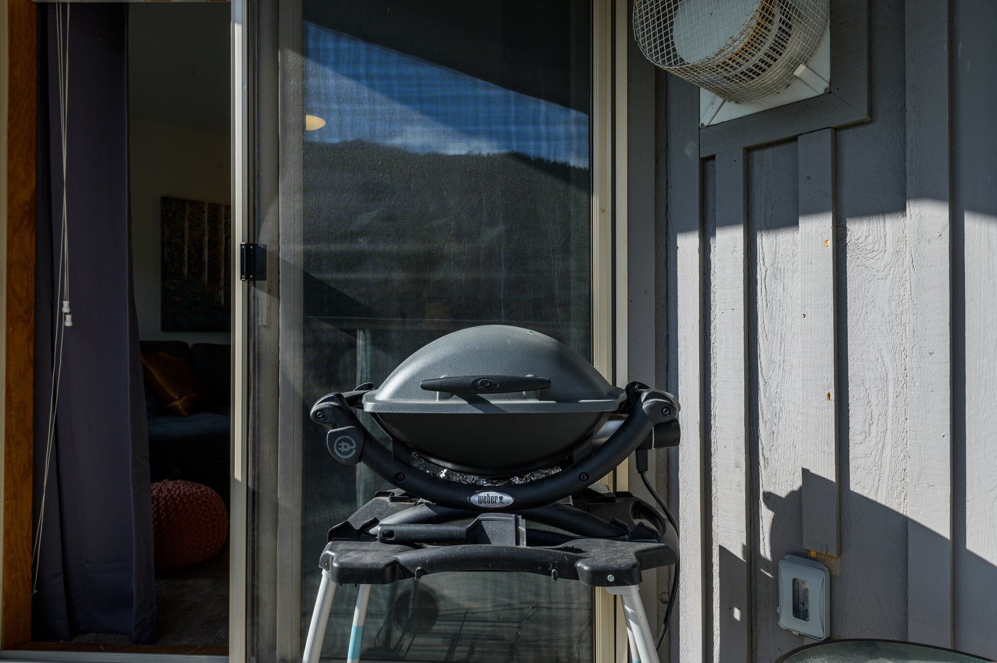 Una parrilla frente a una casa con ventana y un ventilador en la pared.
