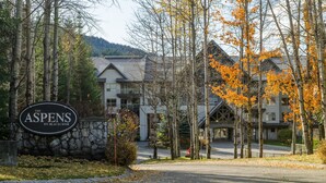 Un chalet avec une entrée surmontée d’un mur en pierre, une enseigne indiquant « The Aspens on Blackcomb », et un bâtiment doté d’un toit en pente.