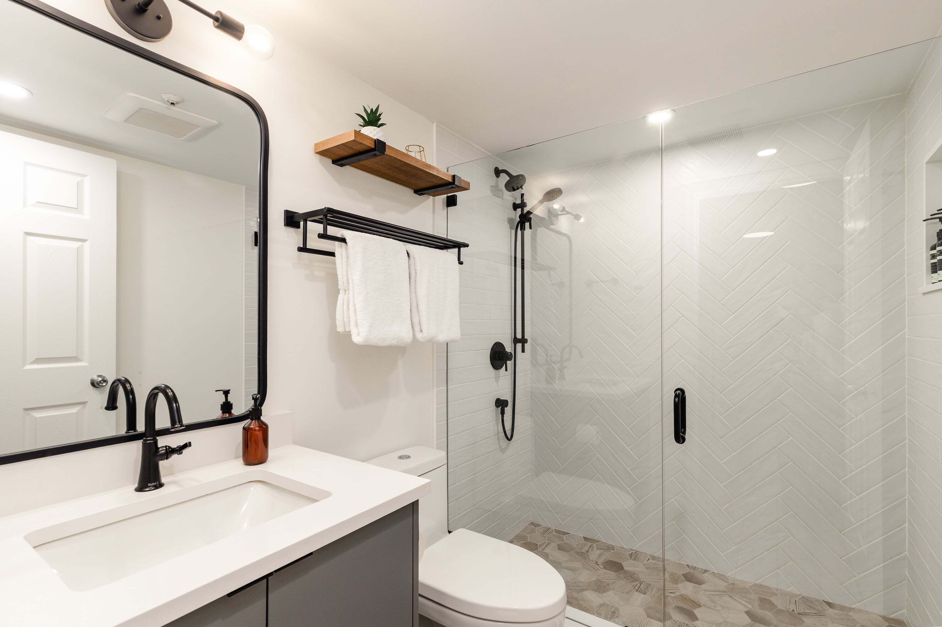 Et moderne badev ærelse med en hvid vask, toilet, bruser med glasvægge og et spejl med håndklædestang over.