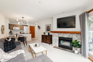 A modern living room with a fireplace, a dining area, and a kitchen in the background. - Panorama Suite at the Aspens (Whistler)