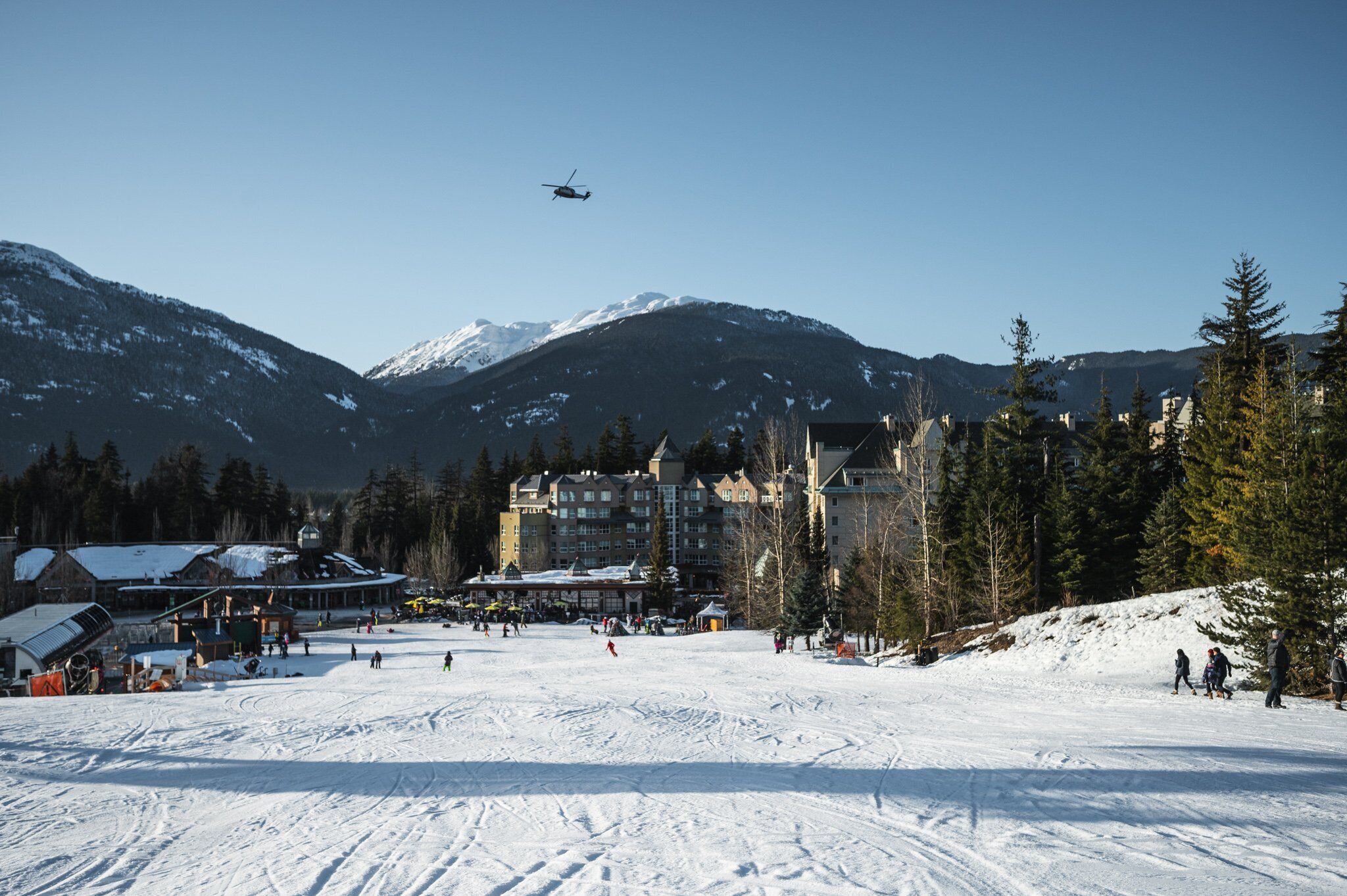 A ski resort with snow-covered slopes, a helicopter, and lodge buildings in the background.