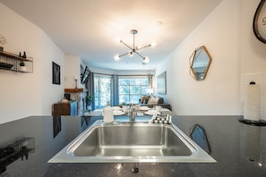 A modern kitchen with a large stainless steel sink, a dining area with a table set for four, and a living room with a sofa and a TV. - Panorama Suite at the Aspens (Whistler)