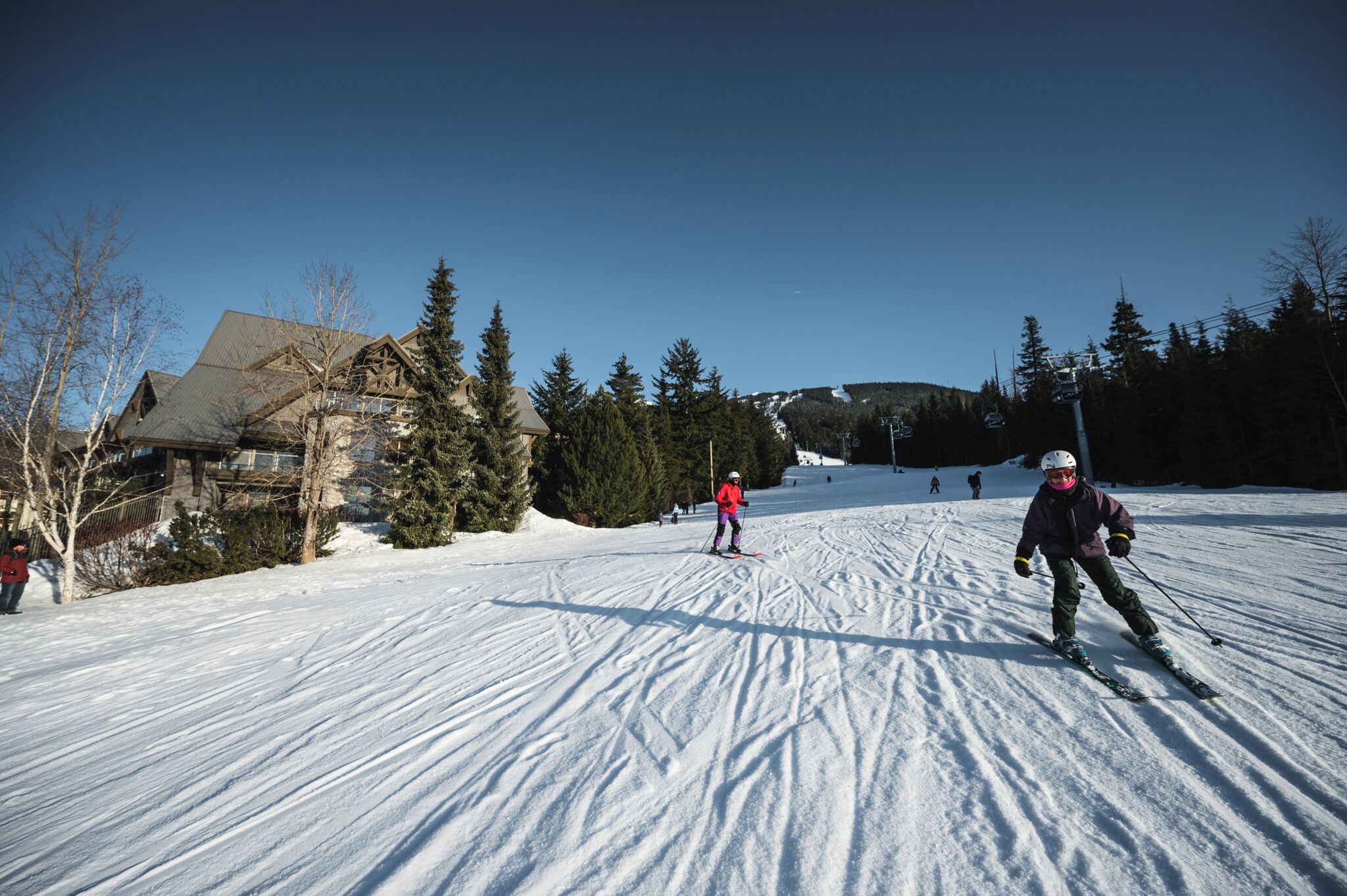 Une piste de ski avec des skieurs, un chalet et une montagne en arrière-plan.
