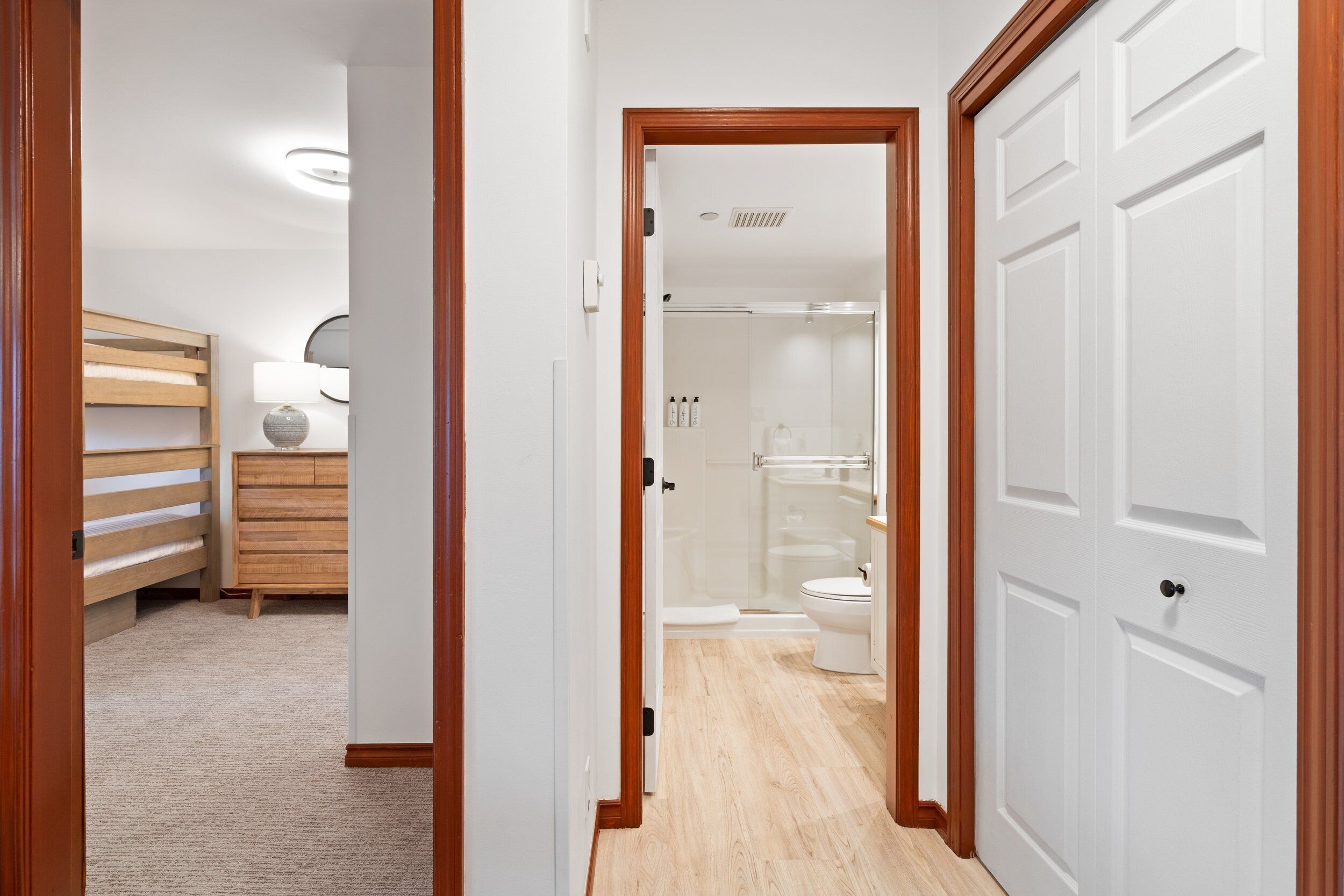 A hallway leading to a bathroom with a shower, toilet, and a wooden bench.