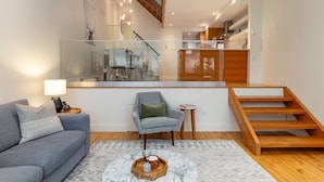 A modern living room with a sofa, a chair, a coffee table, and a staircase leading to an upper level. - Ridgeline Retreat at Sundance (Whistler)