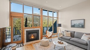 A living room with a fireplace, large windows, a sofa, and a coffee table. - Ridgeline Retreat at Sundance (Whistler)