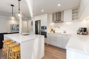 Una cucina moderna con mobili bianchi, elettrodomestici in acciaio inossidabile e un'isola centrale con sgabelli.