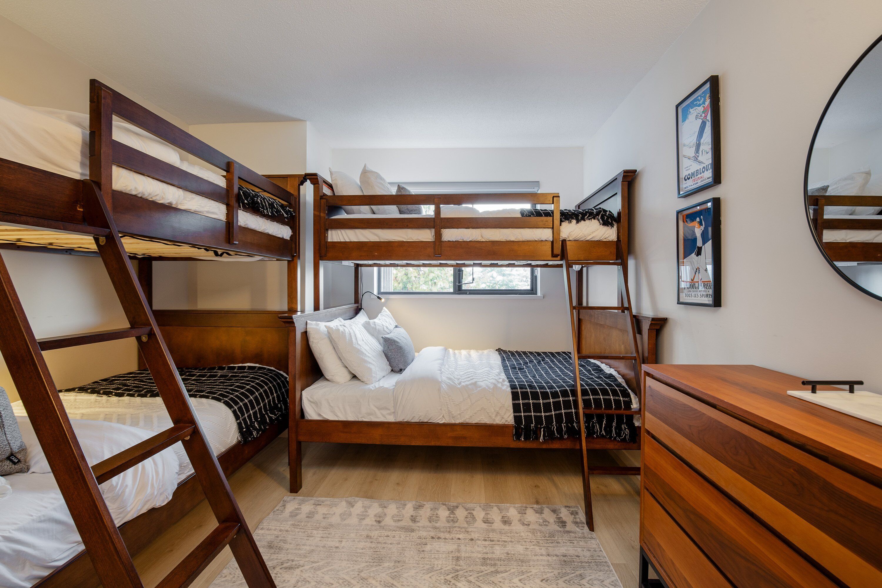 A bunk bed room with a wooden dresser, a mirror, and two framed pictures on the wall.