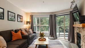 A living room with a sofa, a coffee table, a fireplace, and large windows. - Skywalk Suite at the Aspens (Whistler)