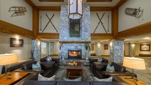 A lobby with stone walls, a fireplace, leather sofas, and a wooden ceiling. - Skywalk Suite at the Aspens (Whistler)