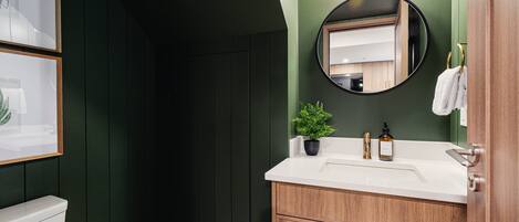 Une salle de bain avec des toilettes blanches, un meuble-lavabo en bois avec un miroir, un évier et une plante en pot.