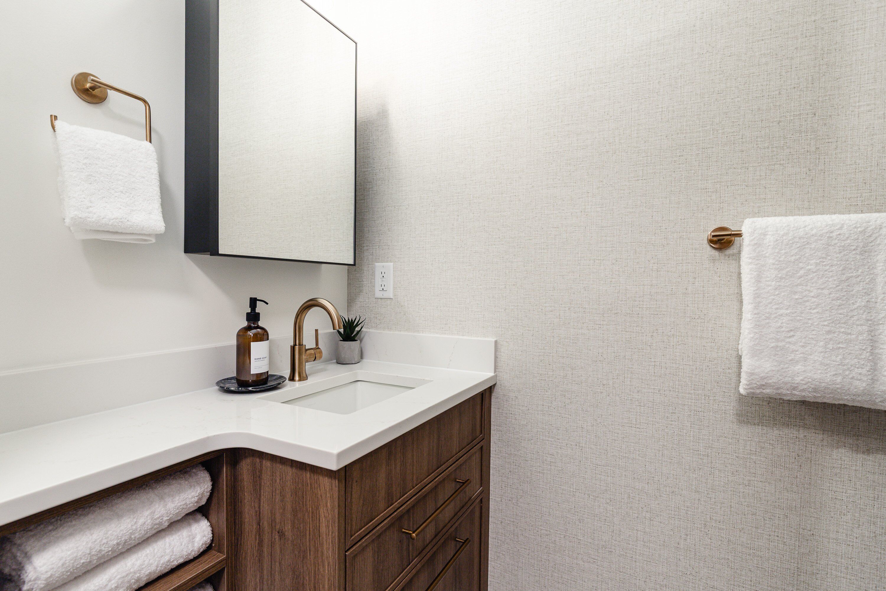 A bathroom with a white sink, wooden vanity, a mirror, and two towels.