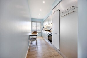 A narrow kitchen with a dining area, white cabinets, a microwave, and a stove.